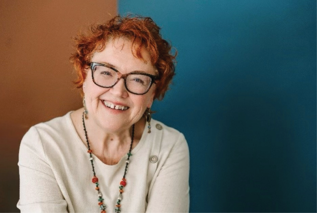 Suzanne facing the camera, divided colorful background, glasses, smiling. 